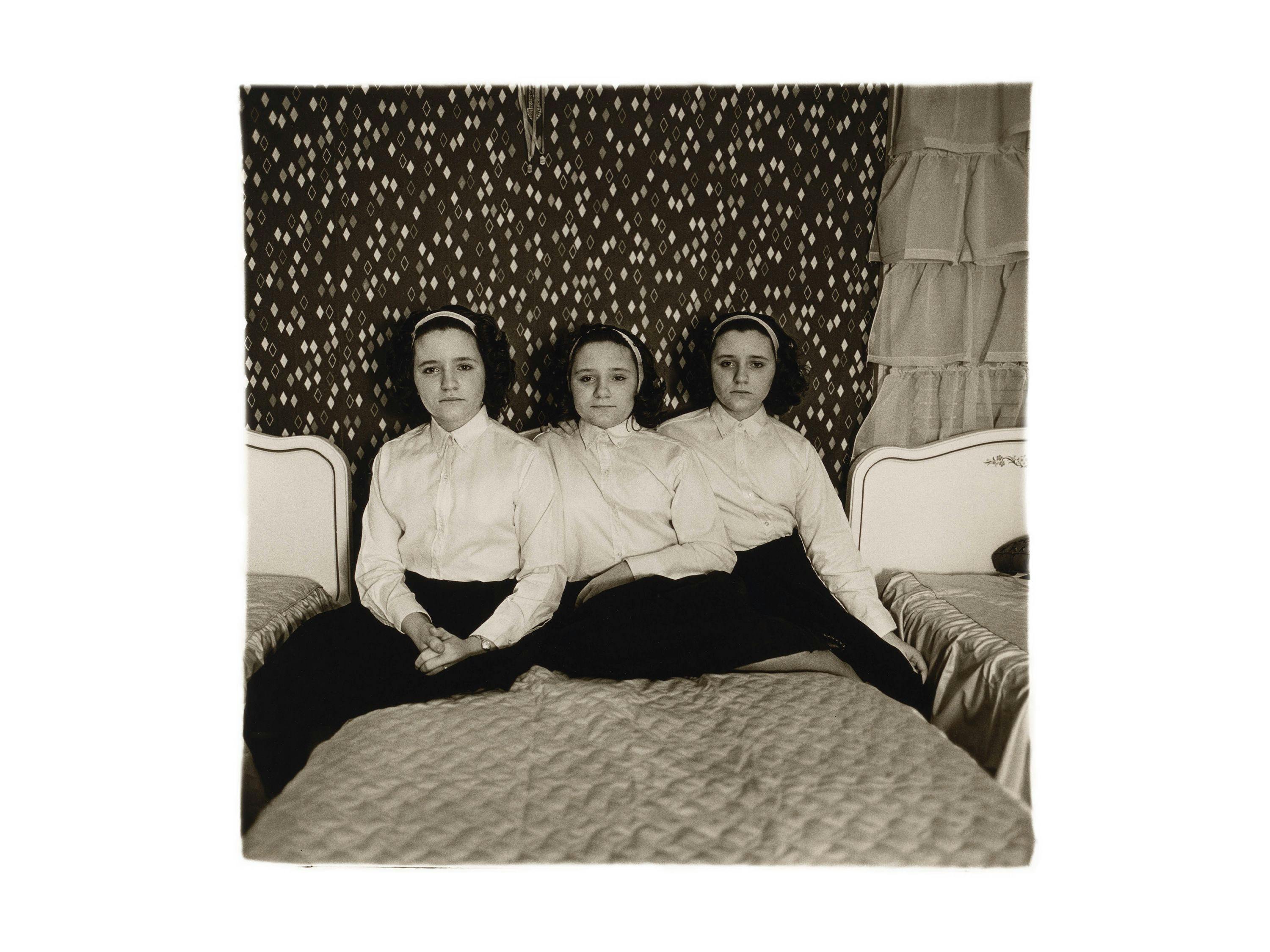 A gelatin silver print by Diane Arbus, titled Triplets in their bedroom, N.J. 1963, dated 1963.